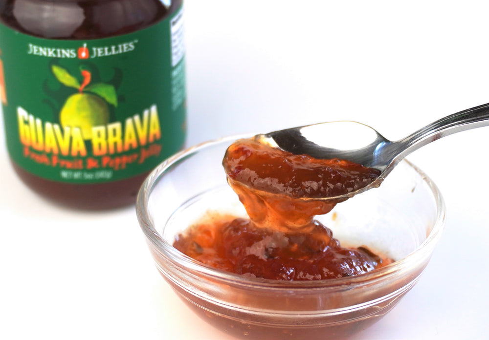 
                  
                    Load image into Gallery viewer, Jenkins Jellies Guava Brava sweet and hot pepper jelly in a bowl with a spoon. Amber colored pepper jelly with fresh chili peppers. Vegan, Gluten and fat free, sweet and spicy hot pepper jam.
                  
                