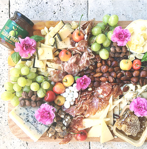 
                  
                    Load image into Gallery viewer, Jenkins Jellies Guava Brava hot pepper jelly is perfect for any charcuterie presentation. Here a 5 oz. jar of the sweet and spicy hot jam sits on a cutting board with an assortment of fresh fruits, nuts, salami and honeycomb. 
                  
                